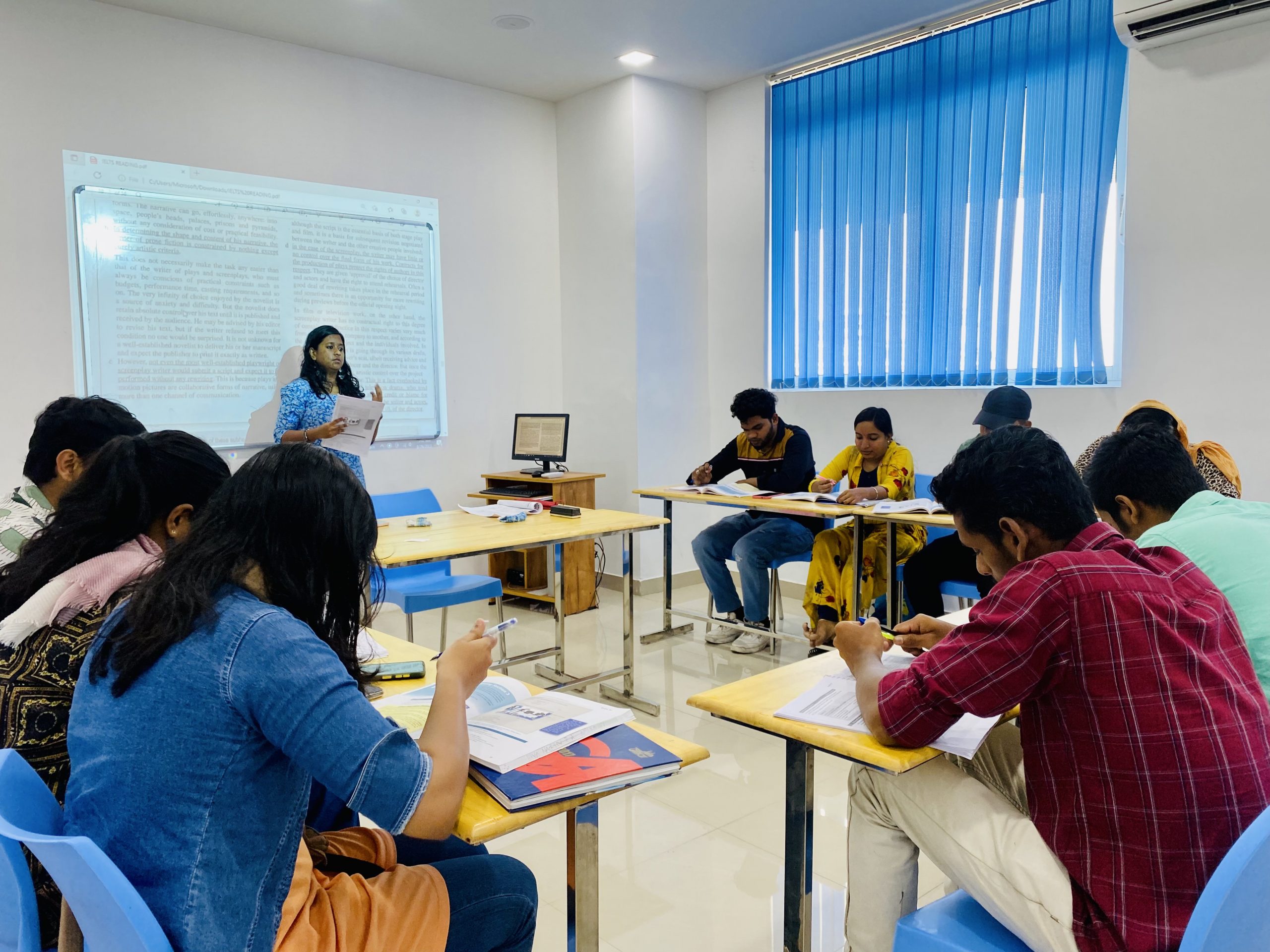 A photo of LearninGuru class room showing a group of students in an IELTS coaching class, with a teacher explaining a concept on a whiteboard.